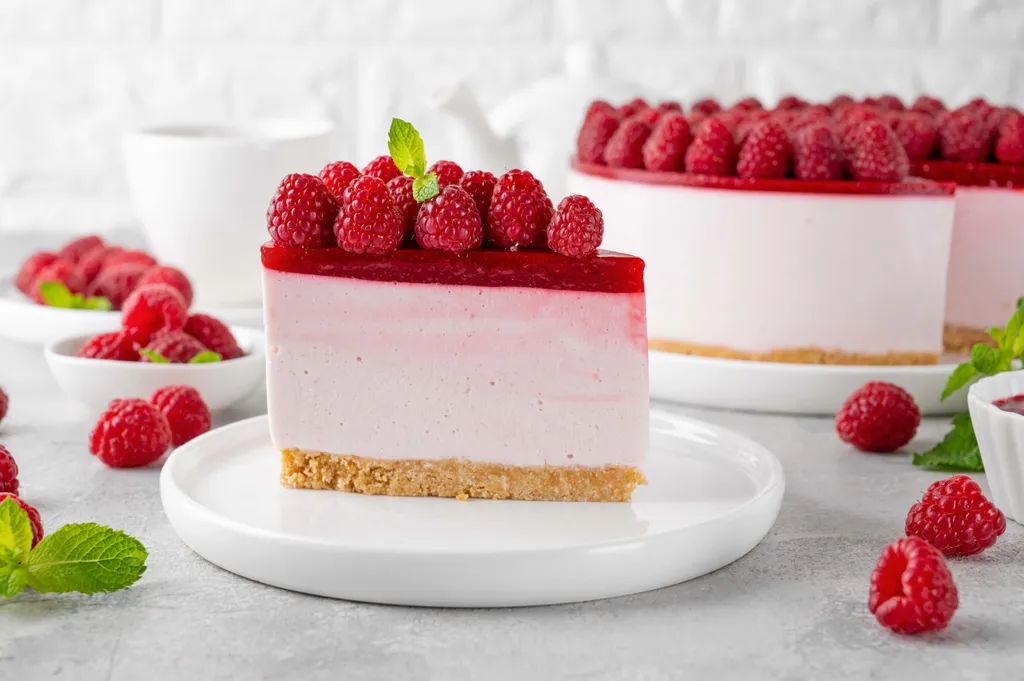Stück Himbeer-Cheesecake mit frischen Himbeeren auf einem weißen Teller