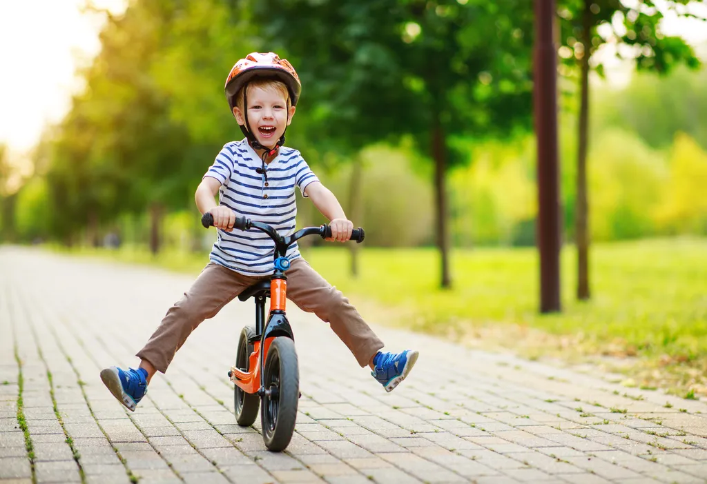 Lachendes Kind mit Helm fährt sicher auf einem Laufrad im Park