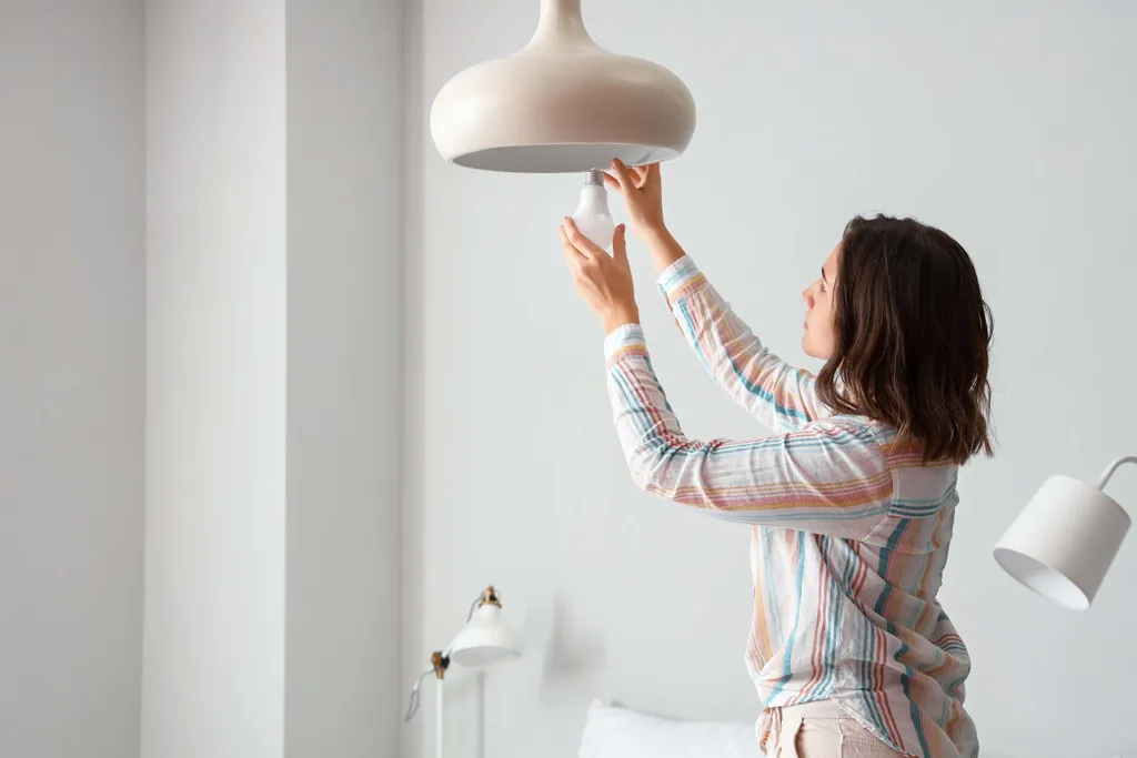 Person wechselt eine LED-Lampe in einer modernen Deckenleuchte im Wohnbereich