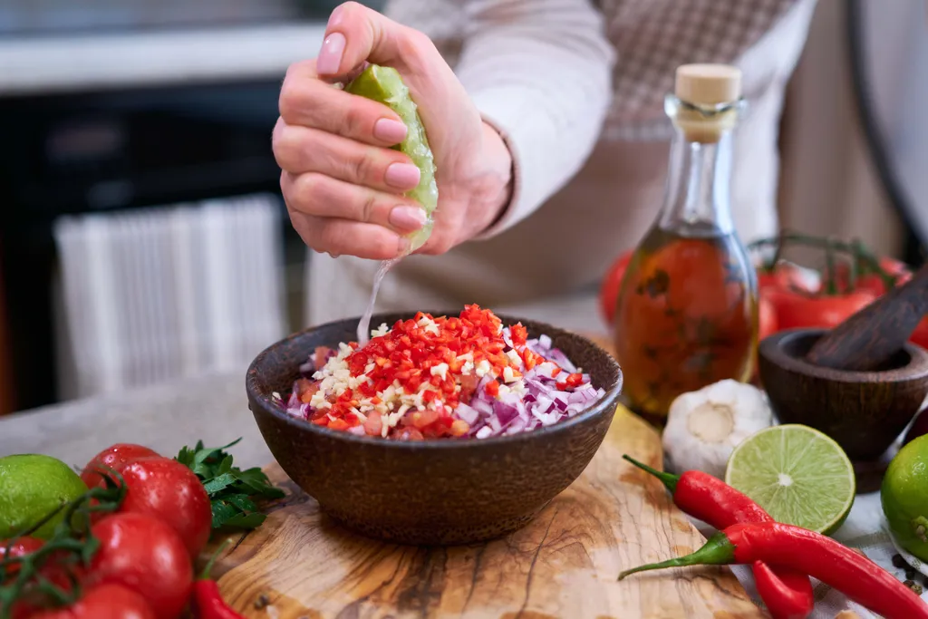 Eine Person presst Limettensaft auf eine Schüssel mit frischen Zutaten für eine Salsa