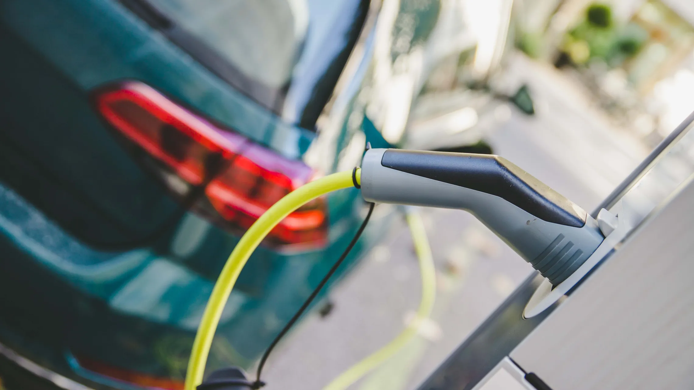 Ein Elektroauto wird über ein gelbes Kabel an einer Ladestation aufgeladen, im Hintergrund ist das Rücklicht des Fahrzeugs zu sehen.