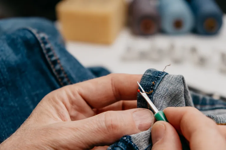 Zwei Hände trennen die Naht einer Jeans auf