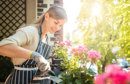 Eine Frau steht am Balkon und pflanzt Blumen.