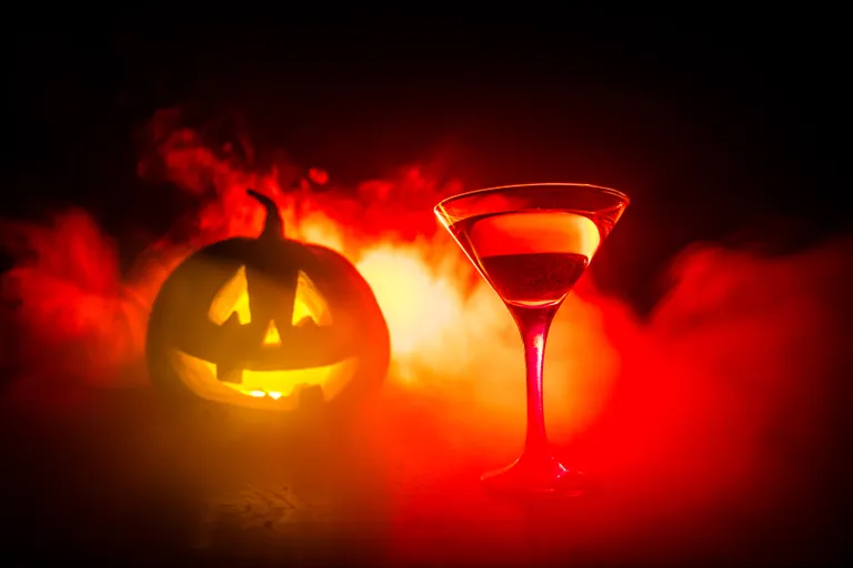 Roter Halloween-Cocktail im Martiniglas vor leuchtendem Kürbis und Nebel