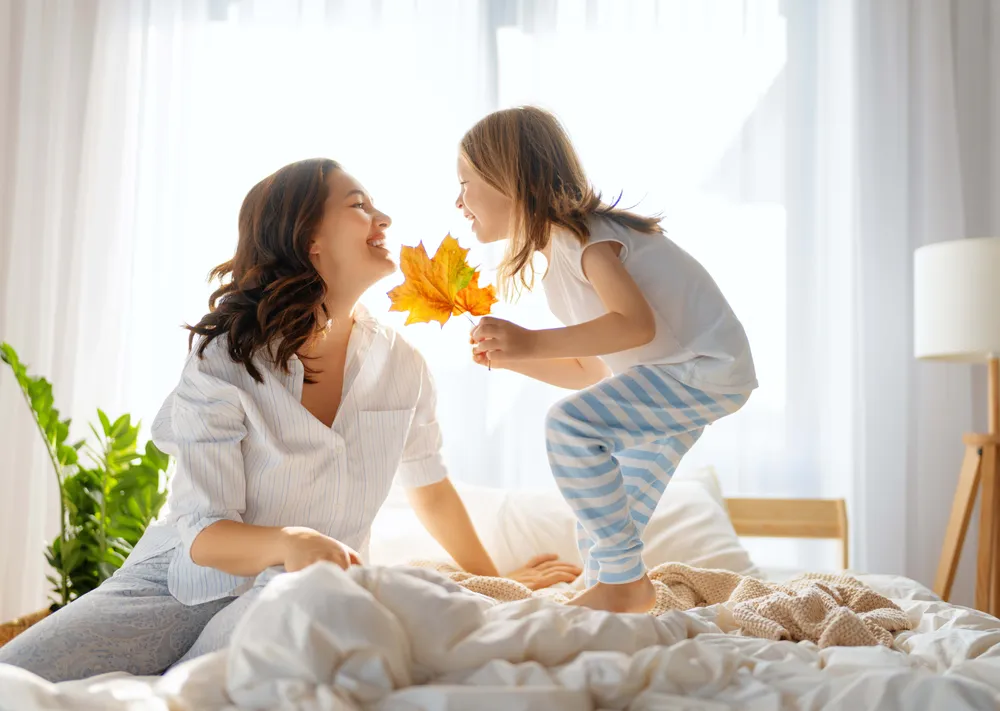 Mutter und Kind sitzen morgens im Bett und halten ein buntes Herbstblatt