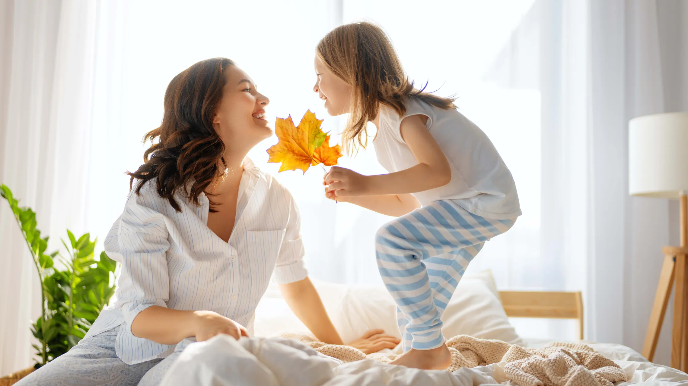 Mutter und Kind sitzen morgens im Bett und halten ein buntes Herbstblatt