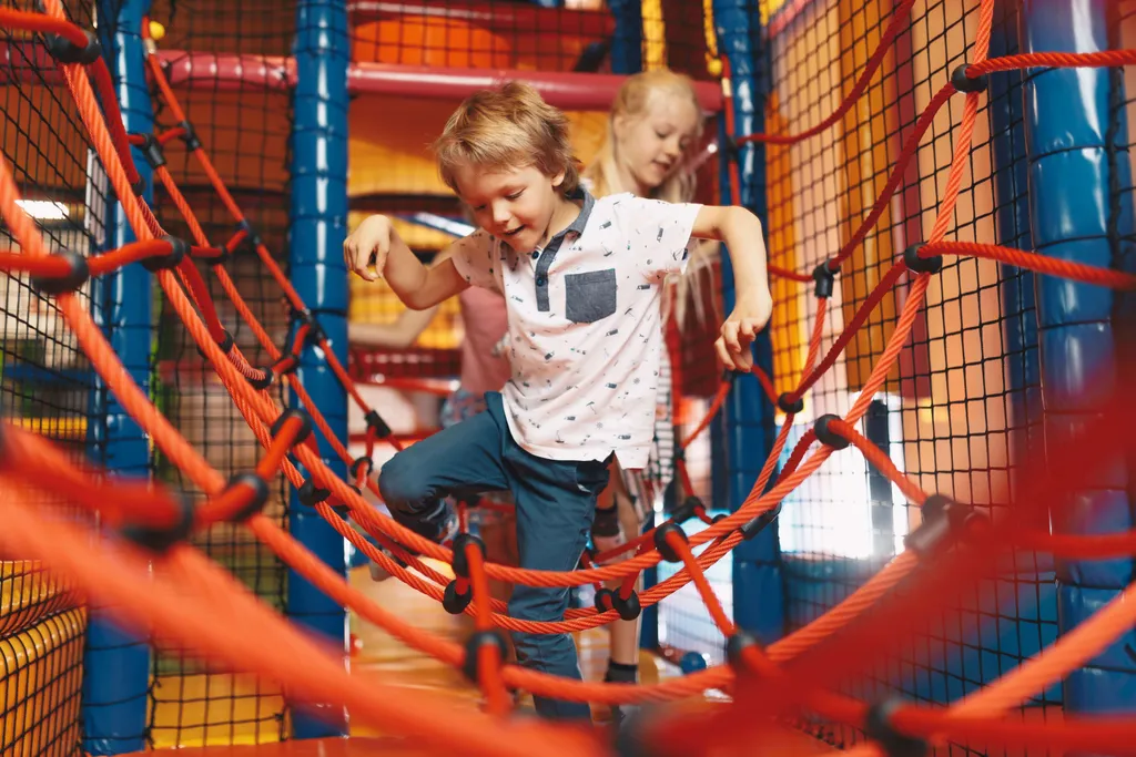 Kinder balancieren auf einem Kletternetz in einem Indoor-Spielplatz