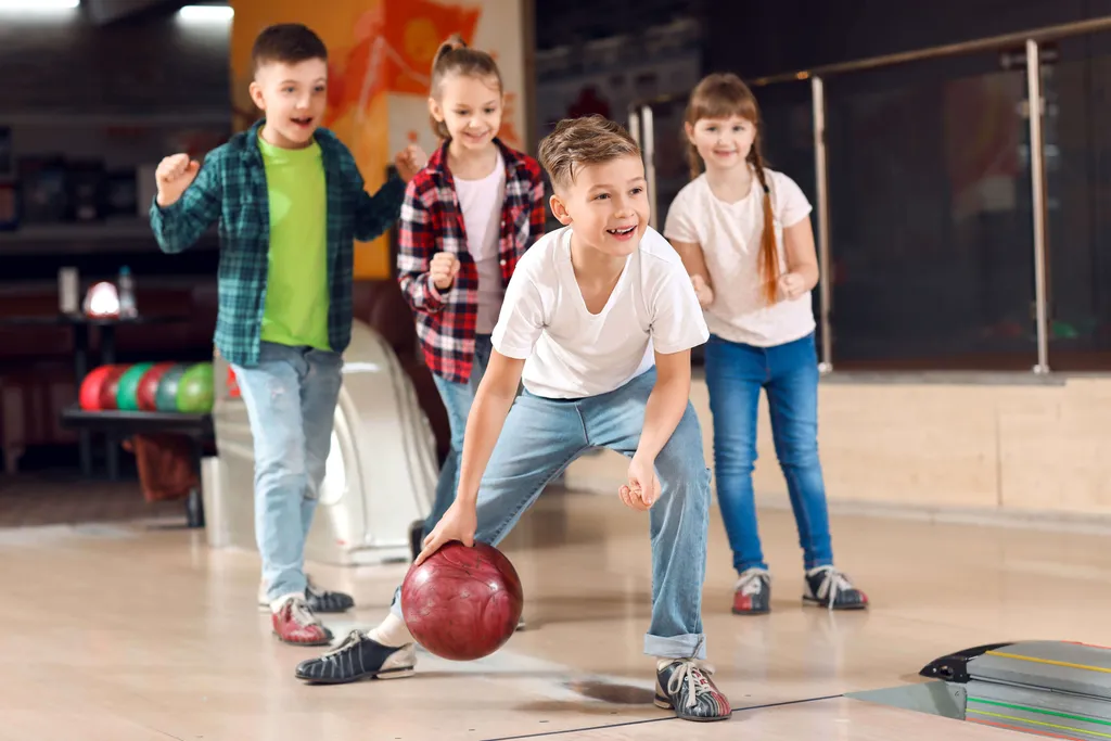 Kinder werfen gemeinsam Bowlingkugeln auf einer Bowlingbahn