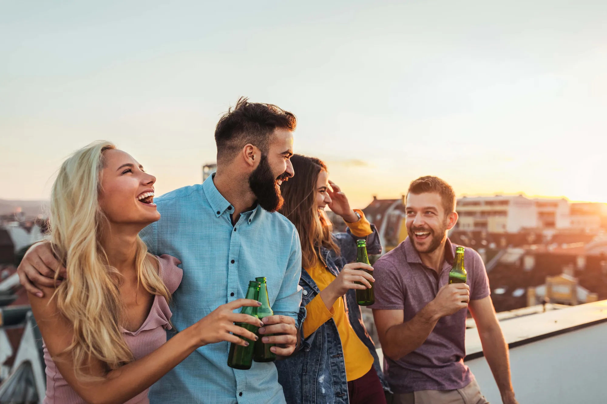 Mehrere Personen beim gemeinsamen Spaß haben und Bier trinken auf einer Dachterrasse im Sonnenuntergang