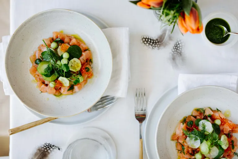 Gurke-Saibling-Ceviche, frischen Kräutern und Fischrogen in zwei Schalen auf einem gedeckten Tisch