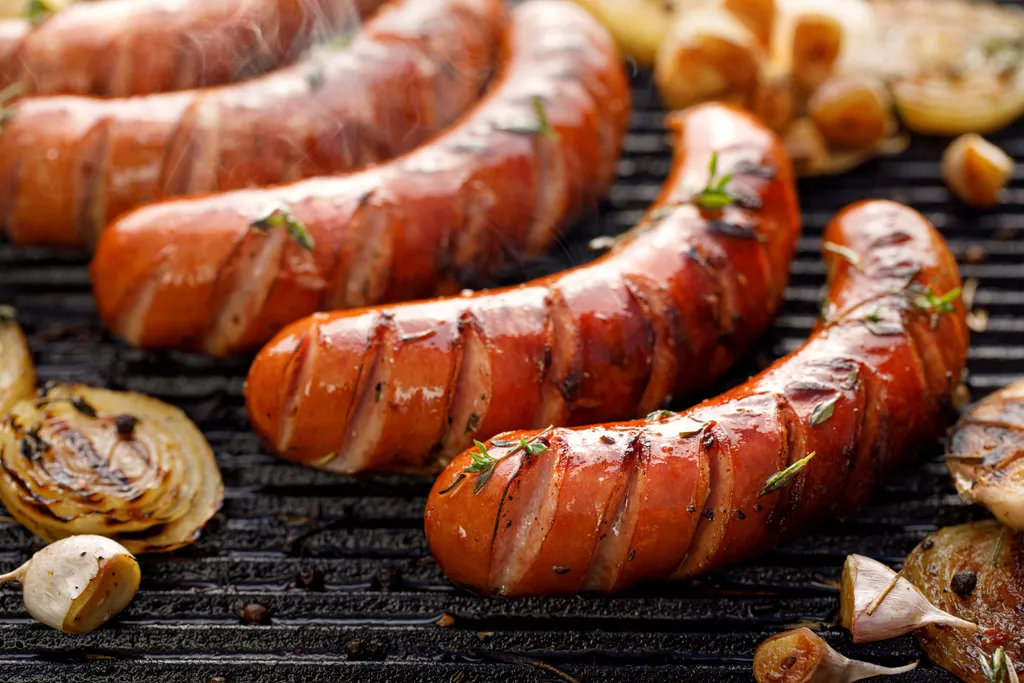 Gegrillte Würstchen mit Kräutern und leicht angebratenen Zwiebelscheiben auf einem Grillrost, die durch ihre appetitliche Konsistenz und ihr verlockendes Aussehen bestechen.