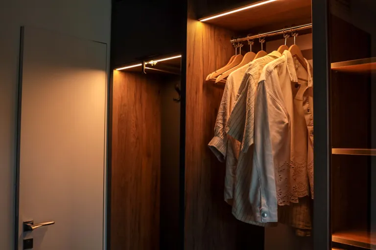 Hemden und andere Kleidungsstücke hängen auf Holzbügeln in einem beleuchteten Kleiderschrank