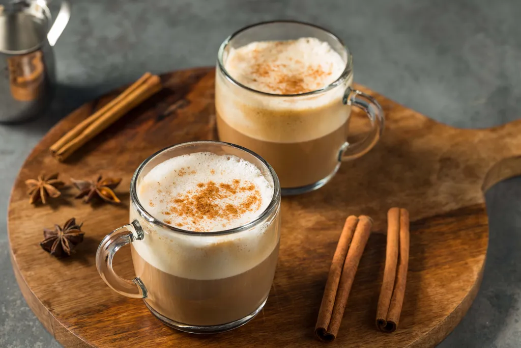 Zwei Cappuccinos mit cremigem Milchschaum und Zimt auf einem Holzbrett.