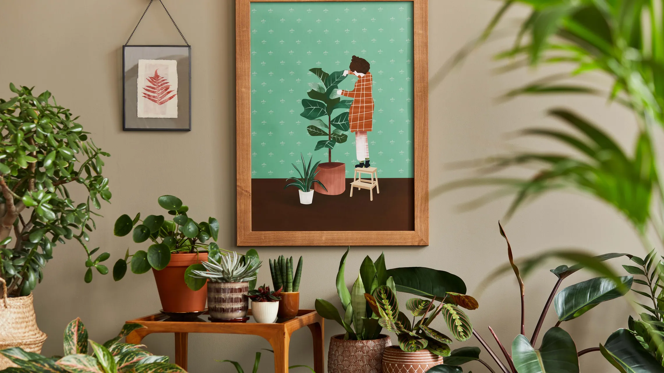 Ein Zimmer mit einer gerahmten Illustration an der Wand, auf der eine Person im Comicstil Zimmerpflanzen pflegt, davor Zimmerpflanzen