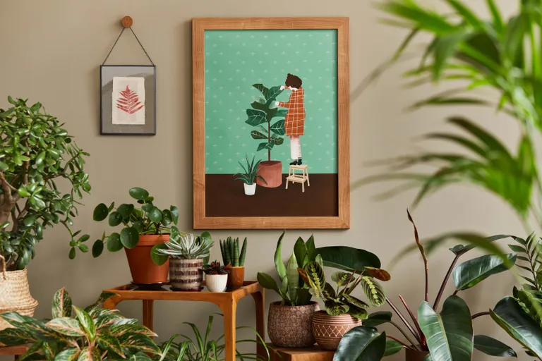 Ein Zimmer mit einer gerahmten Illustration an der Wand, auf der eine Person im Comicstil Zimmerpflanzen pflegt, davor Zimmerpflanzen