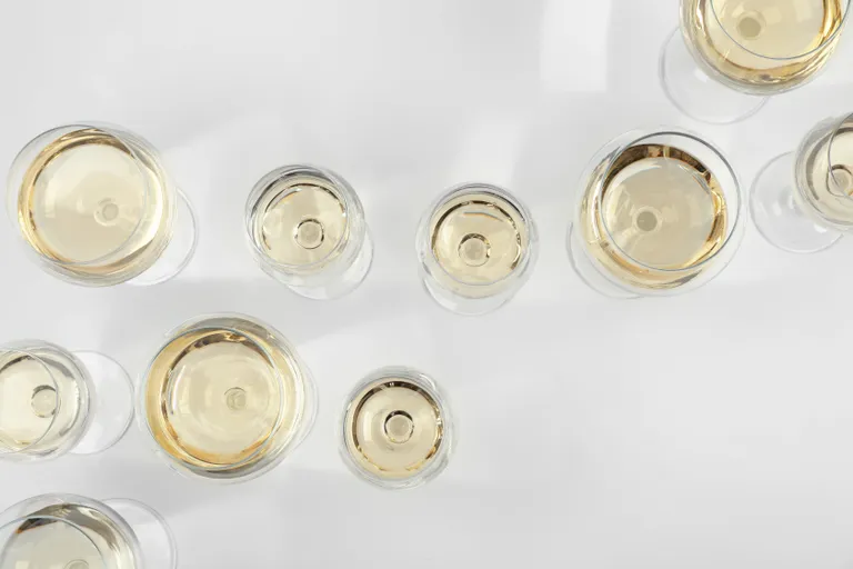 Draufsicht auf mehrere mit Weißwein gefüllte Gläser auf einer weißen Fläche.