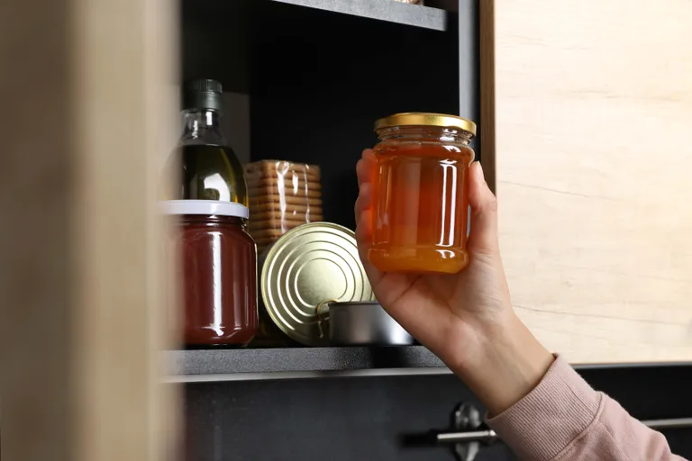 Hand stellt ein Marmeladenglas in den Vorratsschrank