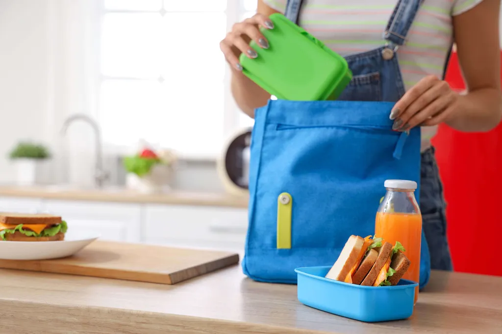 Person packt eine Brotdose mit Sandwich und Getränk in eine Schultasche