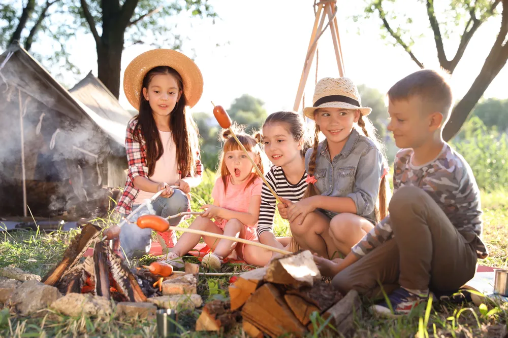 Eine Gruppe Kinder brät Würstchen am Spieß an einem Lagerfeuer