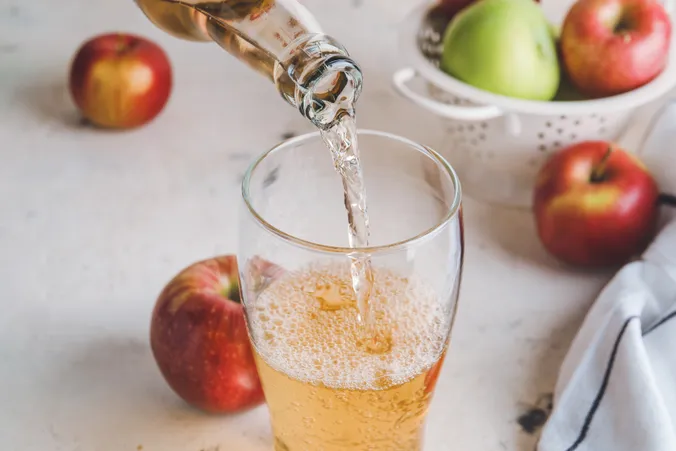 Ein Glas Cider wird gerade eingeschenkt, während im Hintergrund Äpfel zu erkennen sind.
