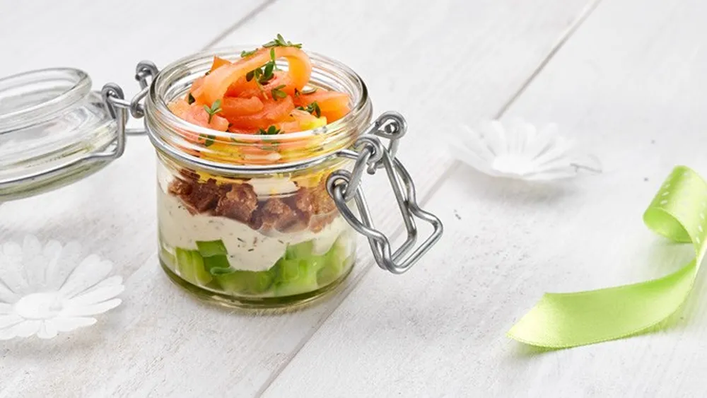 Einmachglas mit Schichten aus Gurke, Frischkäse, Brot und Lachs