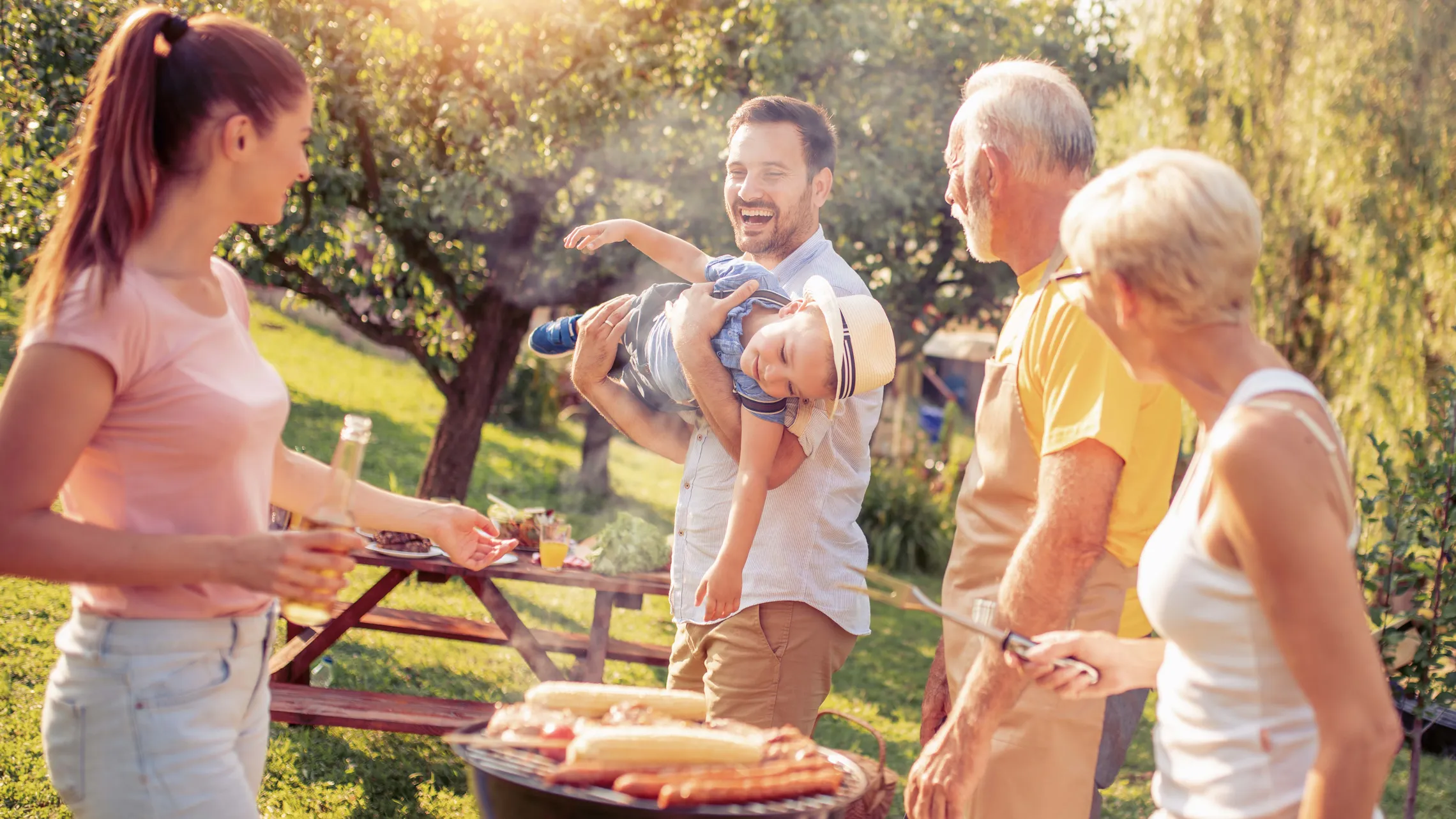 Eine fröhliche Familie beim Grillen in einem sonnigen Garten mit Familienmitgliedern aus mehreren Generationen