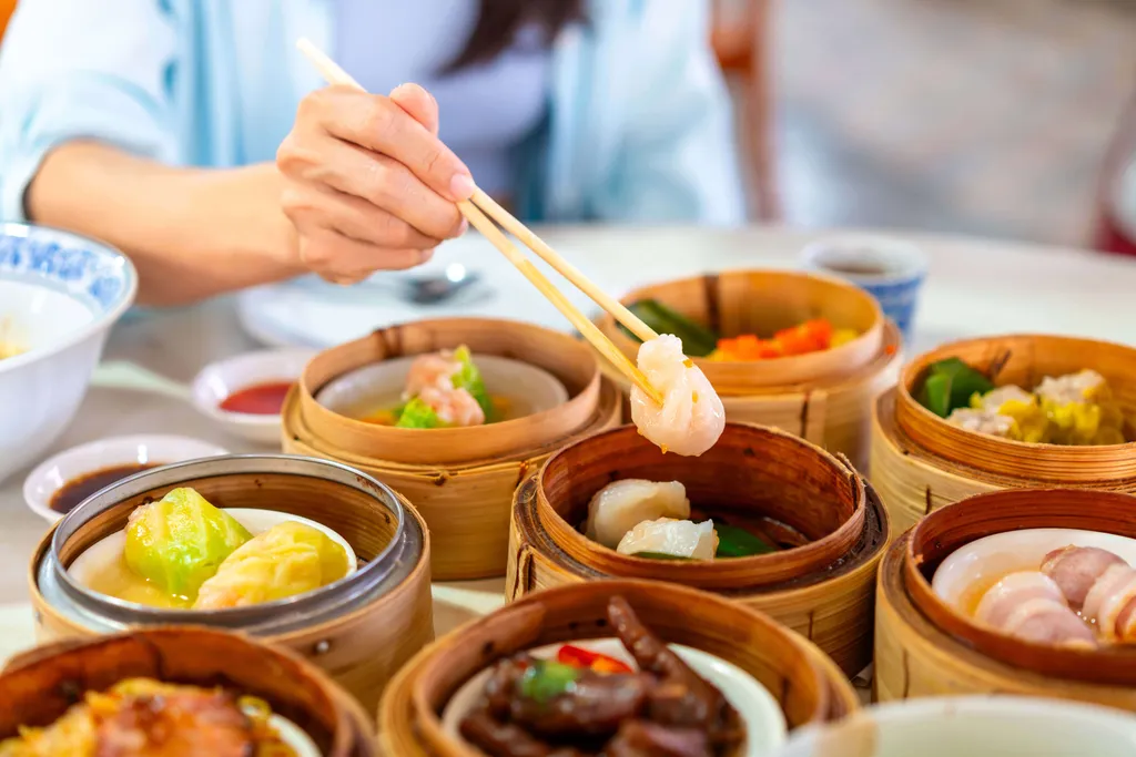 Eine Person genießt verschiedene Dim Sum aus traditionellen Bambuskörben mit Essstäbchen