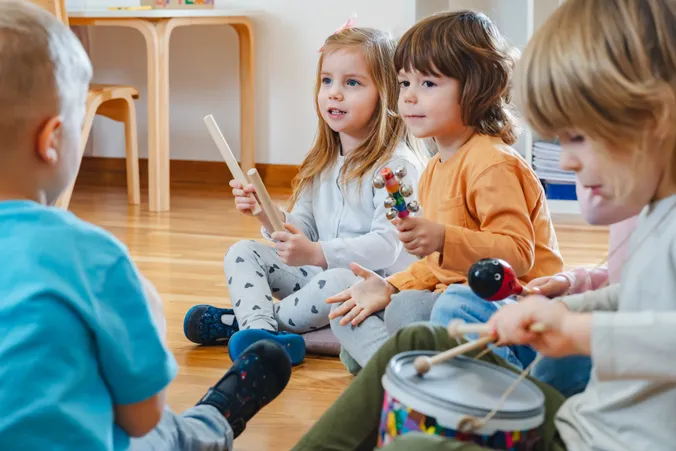 Junge Kinde musizieren am Boden mit Klangstöcken, Rasseln, Trommeln