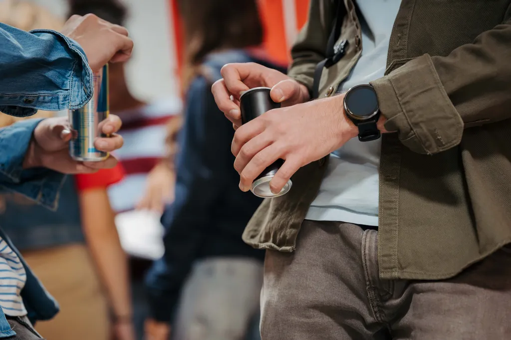 Nahaufnahme von zwei Personen, die Aluminiumdosen in der Hand halten; eine trägt eine blaue Jeansjacke, die andere eine olivgrüne Jacke und eine Smartwatch.