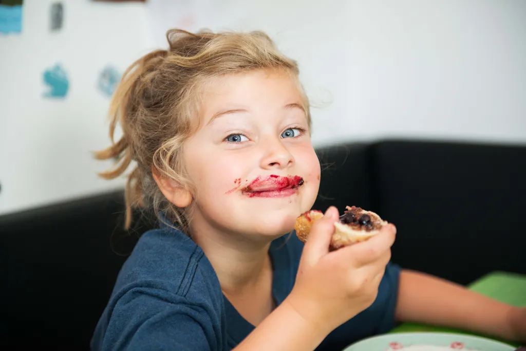 Fröhliches Kind mit Marmelade im Gesicht beim Essen eines Marmeladenbrots