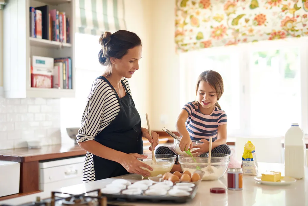 Eine Frau und ein Kind backen gemeinsam in der Küche und rühren Zutaten in Schüsseln um, während Eier und Backzutaten auf der Arbeitsplatte stehen.