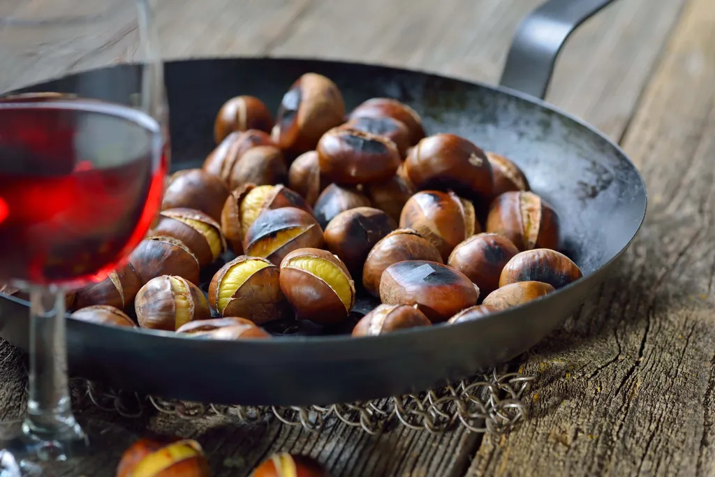 Eine Pfanne mit geröstetetn Maroni und ein Glas Rotweín