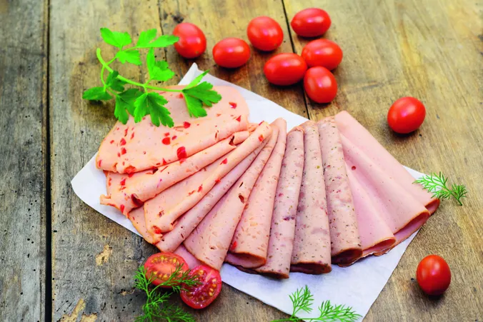 Verschiedene aufgeschnittene Scheiben Wurst auf einem Blatt Papier neben kleinen Tomatem