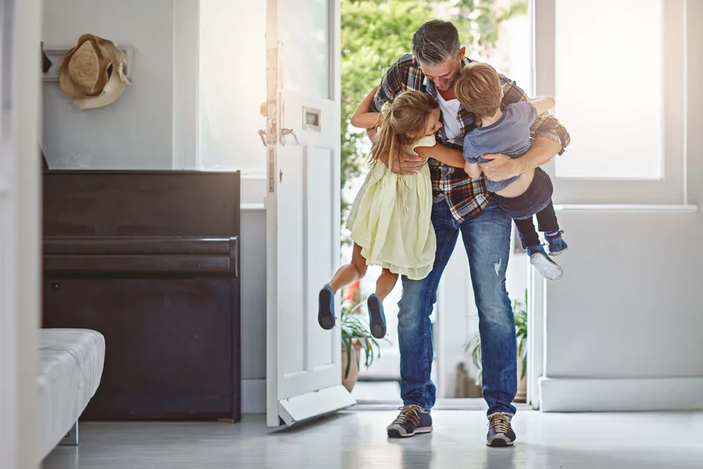 Vater begrüßt und umarmt seine zwei Kinder beim gemeinsamen Ankommen zu Hause