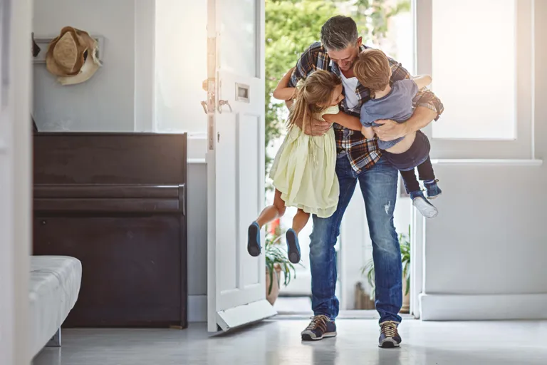 Vater begrüßt und umarmt seine zwei Kinder beim gemeinsamen Ankommen zu Hause