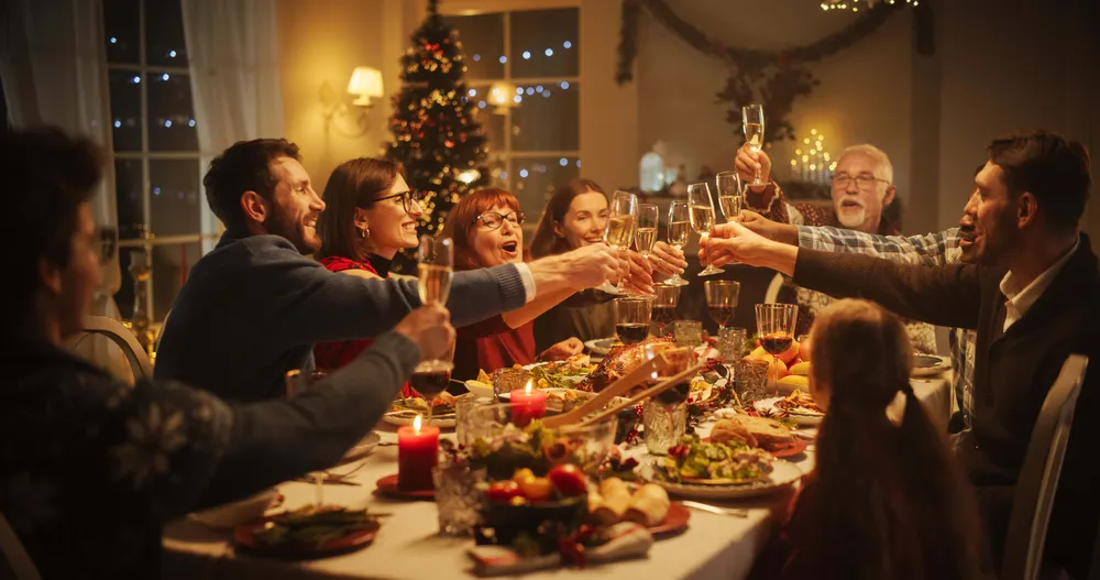 Familie und Freunde stoßen mit Champagner an einem festlich gedeckten Tisch an, der mit Kerzen und Speisen geschmückt ist, in einem warm beleuchteten Raum.