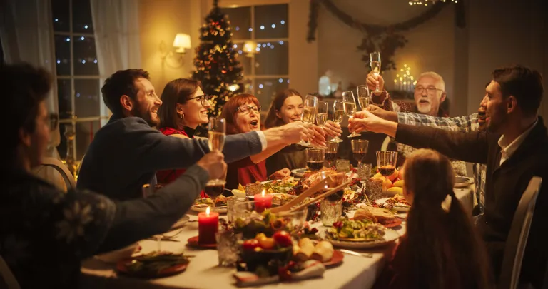 Familie und Freunde stoßen mit Champagner an einem festlich gedeckten Tisch an, der mit Kerzen und Speisen geschmückt ist, in einem warm beleuchteten Raum.