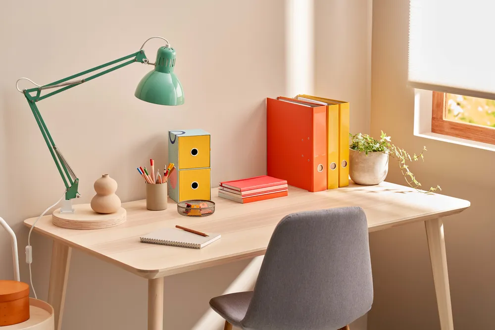 Heller und aufgeräumter Schreibtisch mit Lampe, Büchern und Schreibutensilien als Lernplatz