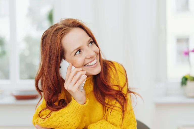 Lächelnde Frau in einem gelben Pullover führt ein Telefonat und informiert
