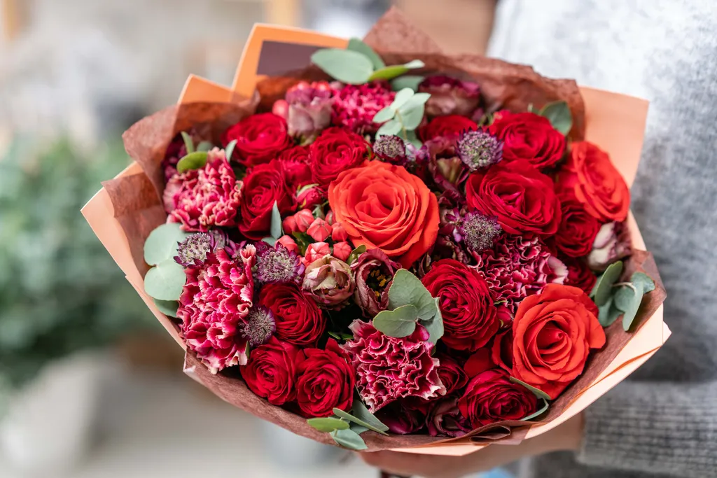 Ein üppiger Blumenstrauß in Rottönen mit Rosen, Nelken, Eukalyptus