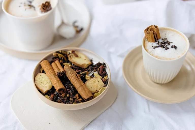 Cremiger Chai Latte mit Zimt und Gewürzen neben einer Schale mit Chai-Mischung