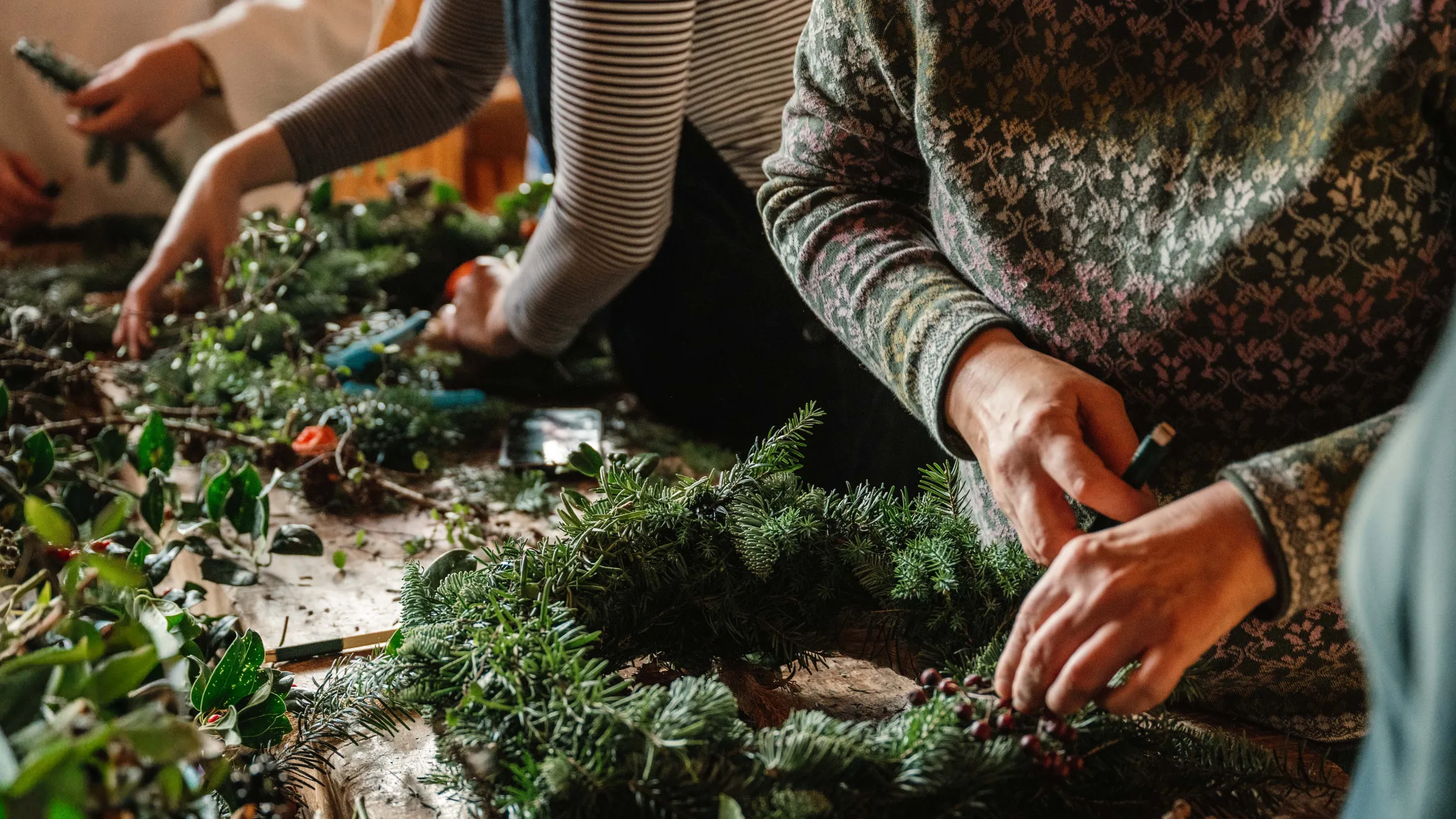 Personen binden gemeinsam einen Adventskranz aus Tannenzweigen und winterlichem Grün