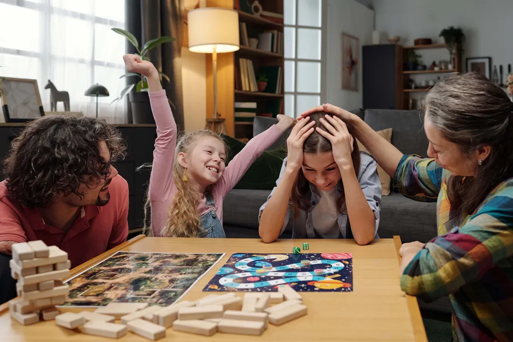 Familie sitzt lachend am Wohnzimmertisch und spielt gemeinsam ein Brettspiel
