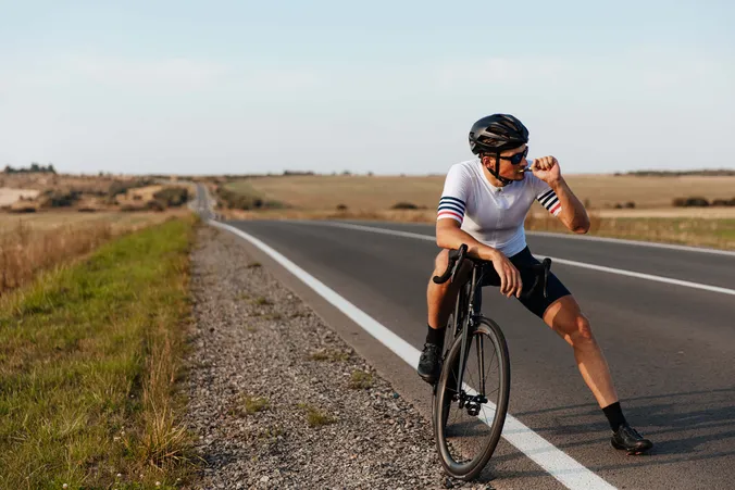 Rennradfahrer macht Pause am Straßenrand und isst einen Energieriegel während einer Ausfahrt