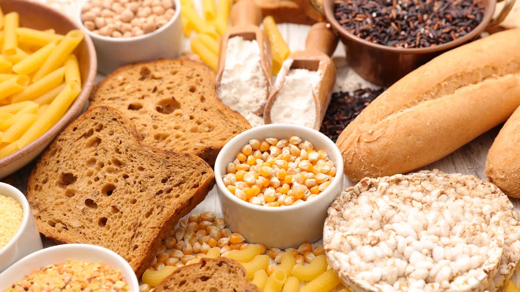 Verschiedene glutenfreie Kohlenhydrate: Nudeln, Brot, Mehl, Maiskörner, Reiskuchen und Getreide, auf einem Tisch ausgestellt.