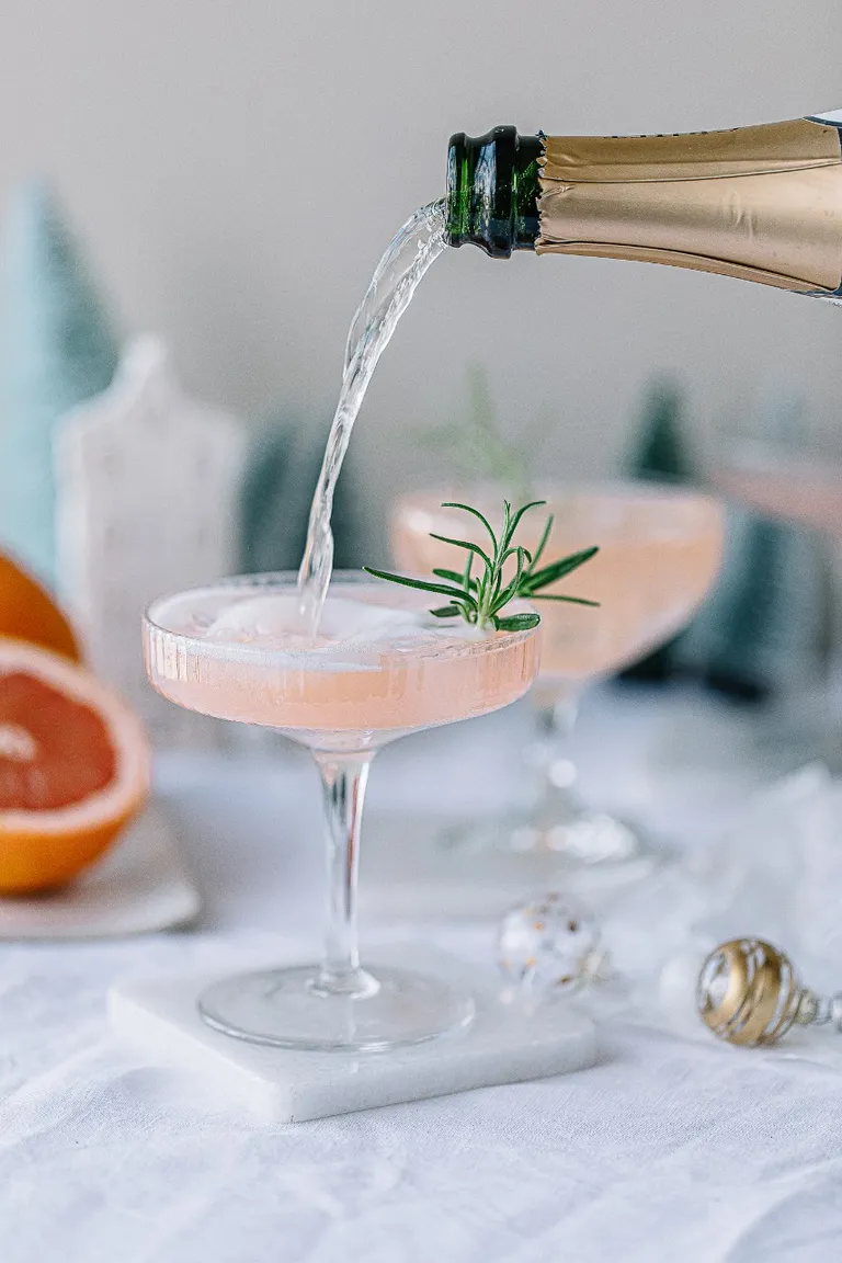 aus einer Flasche Schaumwein wird in ein mit rosa Cocktail gefülltes Cocktailglas nachgeschenkt