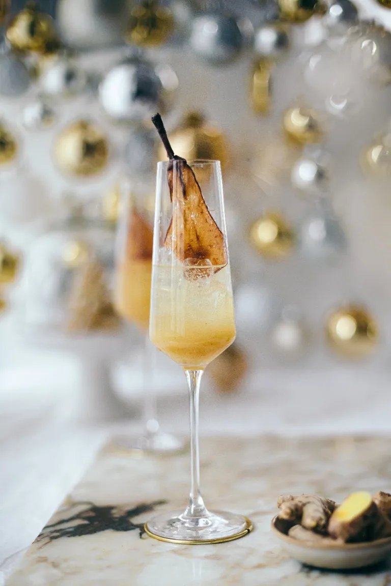 Ein Glas Ingwer Birnen Fizz mit getrockneter Birnenscheibe vor festlichem Hintergrund