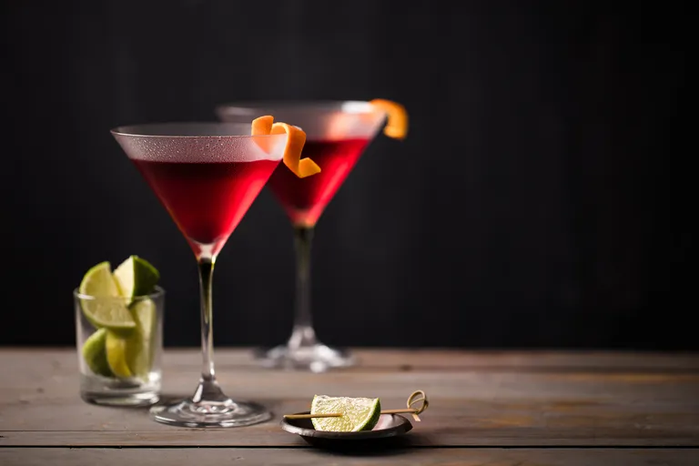 Zwei Cosmopolitan-Cocktails im Martini-Glas mit Orangenzeste und Limettenspalten