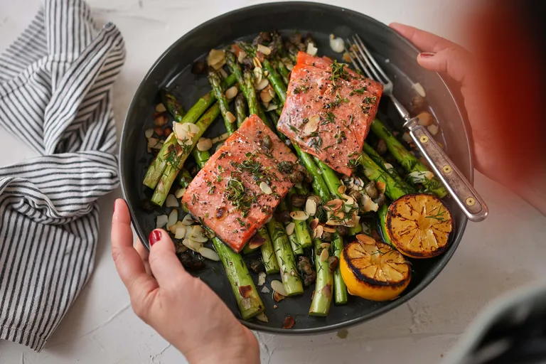 Gebratene Lachsfilets mit grünem Spargel, gerösteten Mandeln und gegrillter Zitrone auf einer Servierplatte