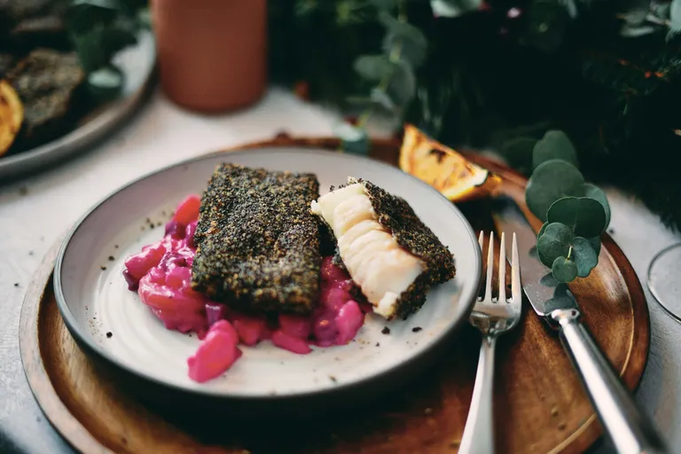 Ein frisch zubereitetes Karpfengfilet im Mohnmantel mit Erdäpfel-Rüben-Salat auf einem gräulichen Teller